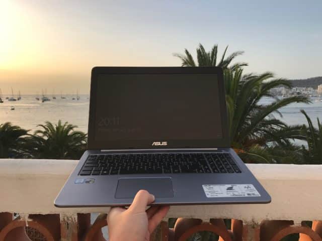 Hand Holding Laptop In Front Of Tropical Ocean