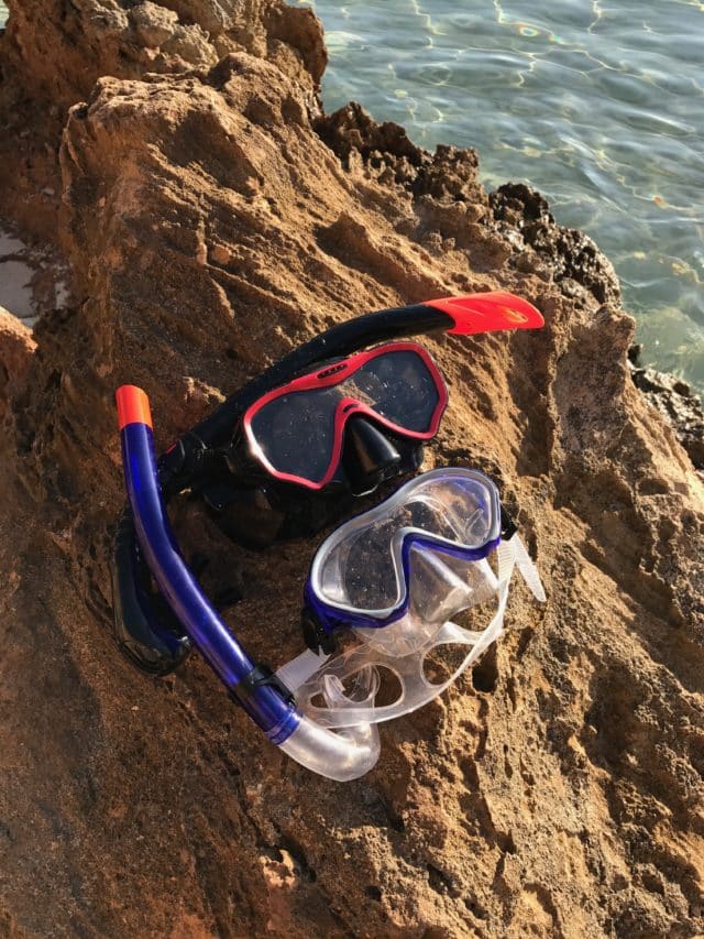 Two Sets Of Diving Goggles And Gear On Rock By Ocean