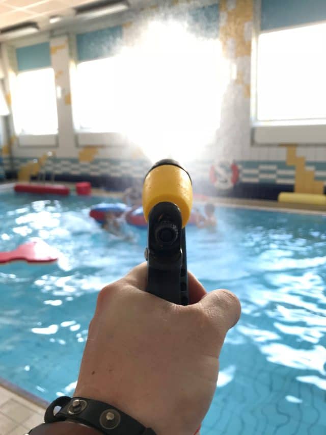 Hand Holding Water Gun Spraying Swimmers In Pool