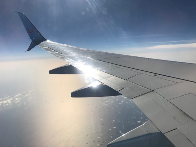Plane Window View Of Wing Over Sea With Clouds