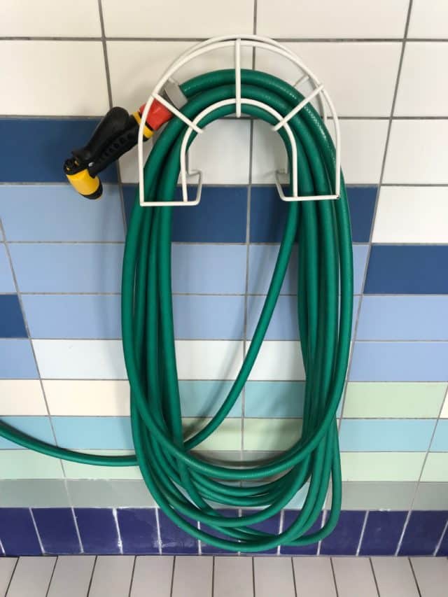 Rolled Up Green Water Hose Hanging On Tiled Wall