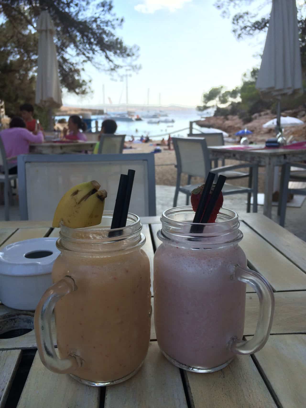 Banana Smoothie And Strawberry Smoothie With Straw On A Wooden Table With Beach As Background