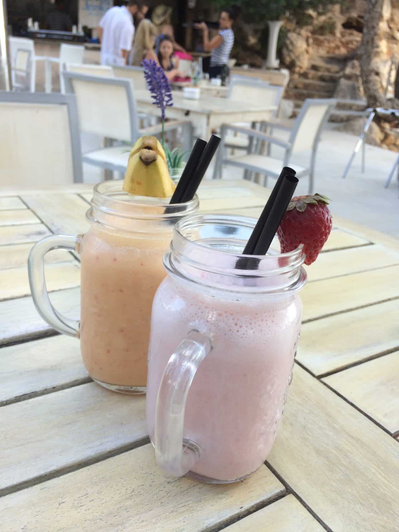 Yellow And Pink Smoothies With Banana Fruit On Glass Edge With People And Flower Background