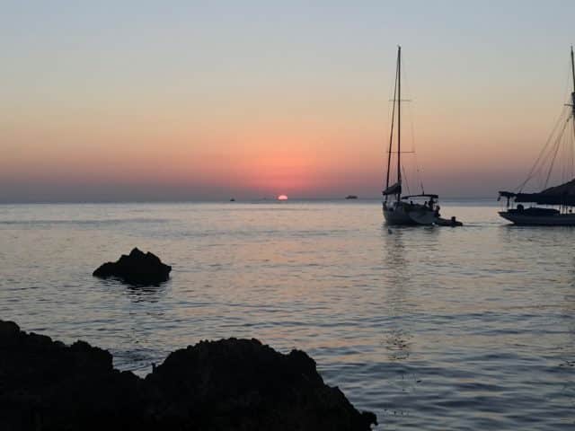 Sunset On A Spanish Beach With Rocks And Boats