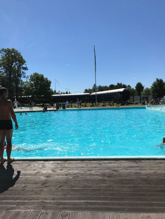 Pool With People And A Train In The Background One Summer Day