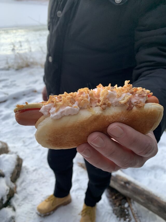 Hand Holding A Hot Dog With Roasted Onion And Shrimp Salad