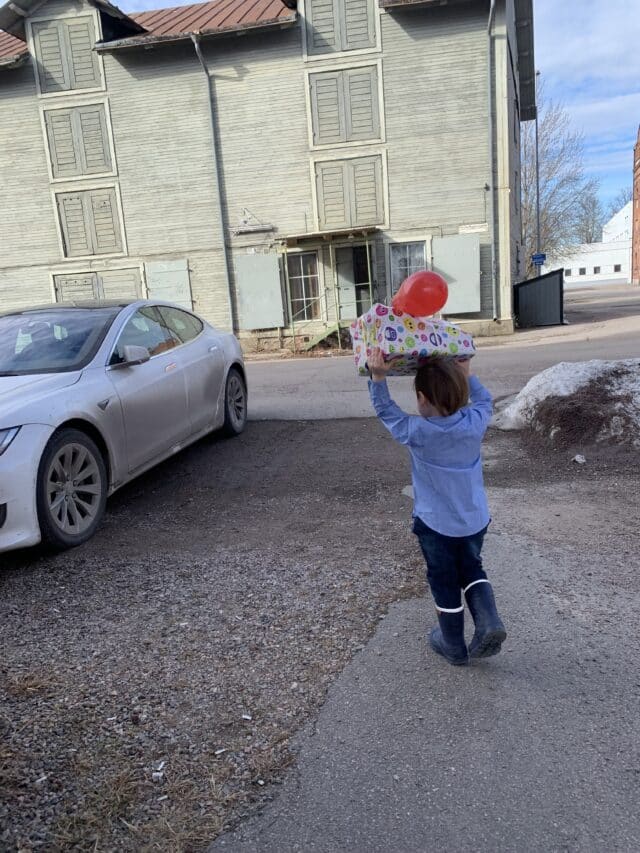 Child Carrying Birthday Present With A Balloon To A Tesla Car