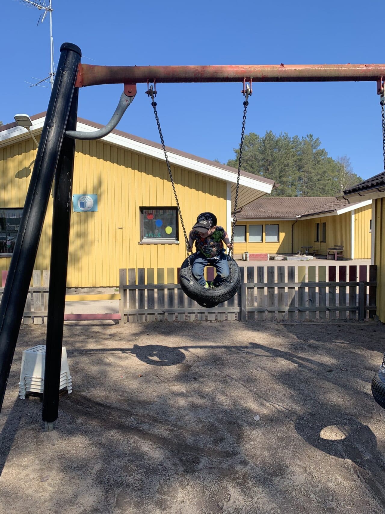 Child Playing In Kindergarten Enclosure On A Swing Set