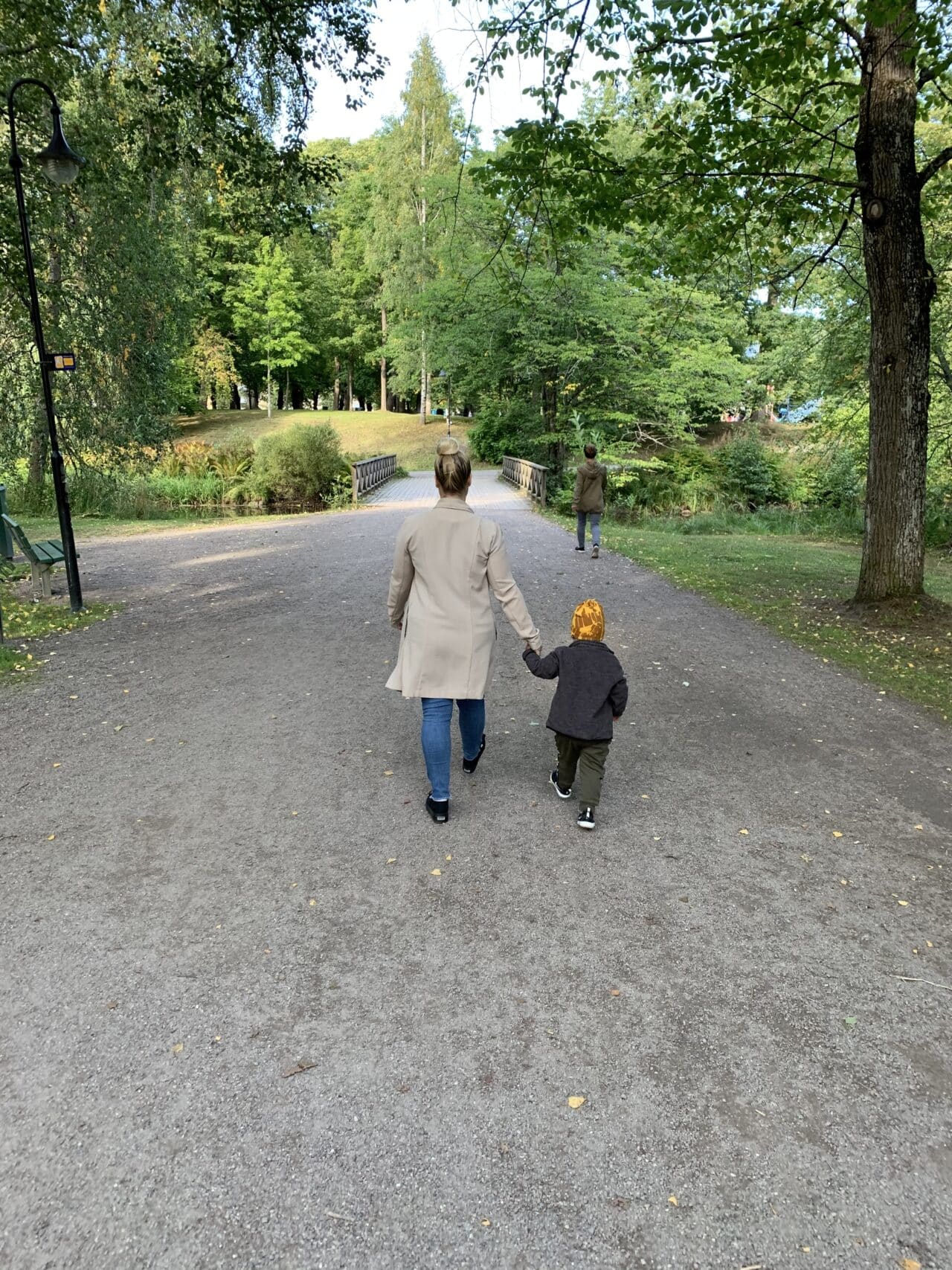 Mother Holding Child And Walking On Gravel Path In Park