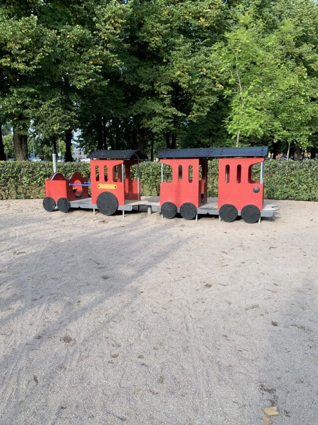 A Red Locomotive With Train Carriages In A Playground