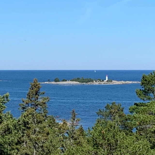 Sea And Island With A Lighthouse And Boat On The Horizon