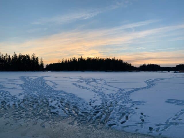 Sunset By A Frozen Lake With Footprints In The Snow