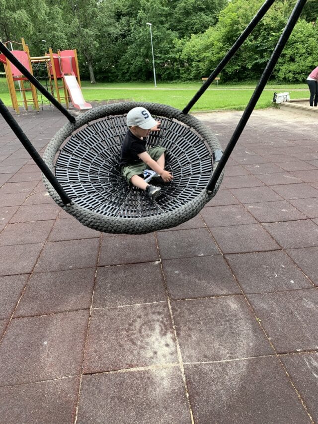 Child with Cap Swings on Friends Swing In Playground